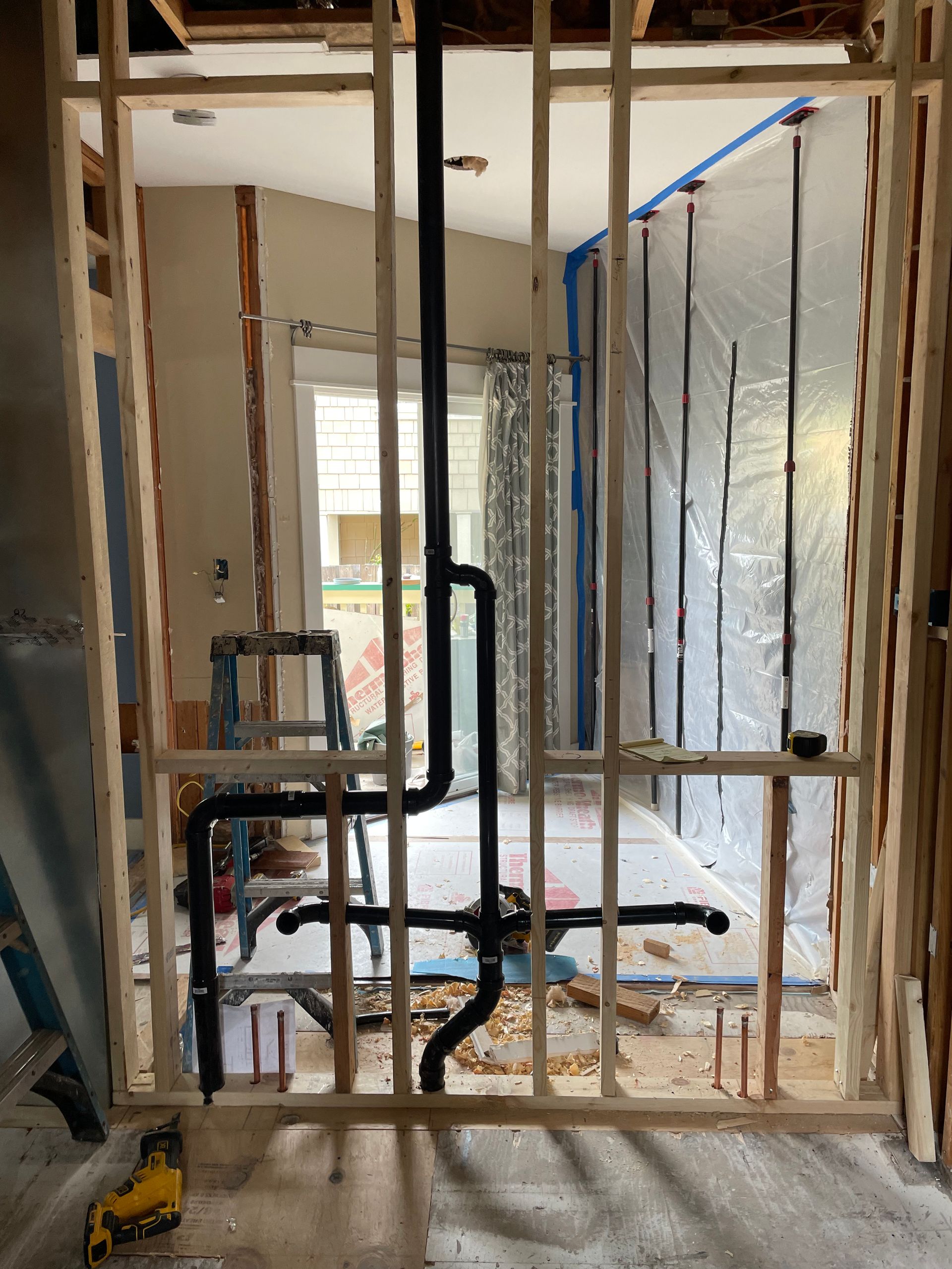 Framed interior wall with a doorway, ladder, and drywall tools at a construction site