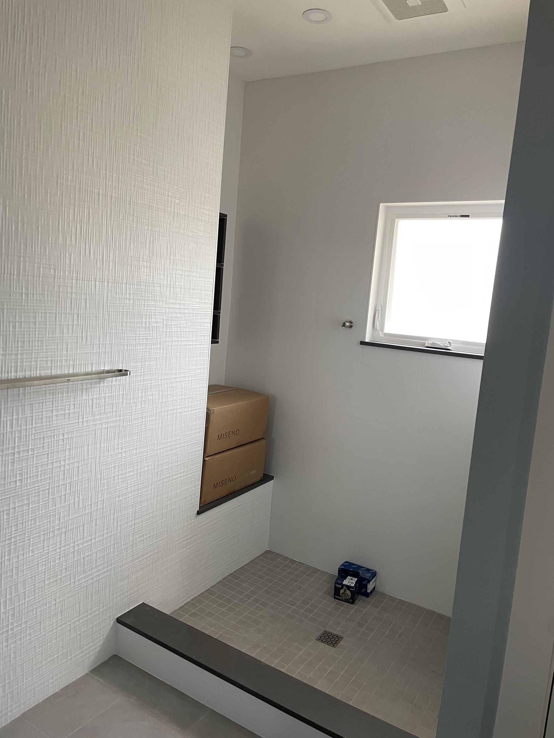Small tiled bathroom with a shower area, white walls, a window, and a wooden vanity cabinet.