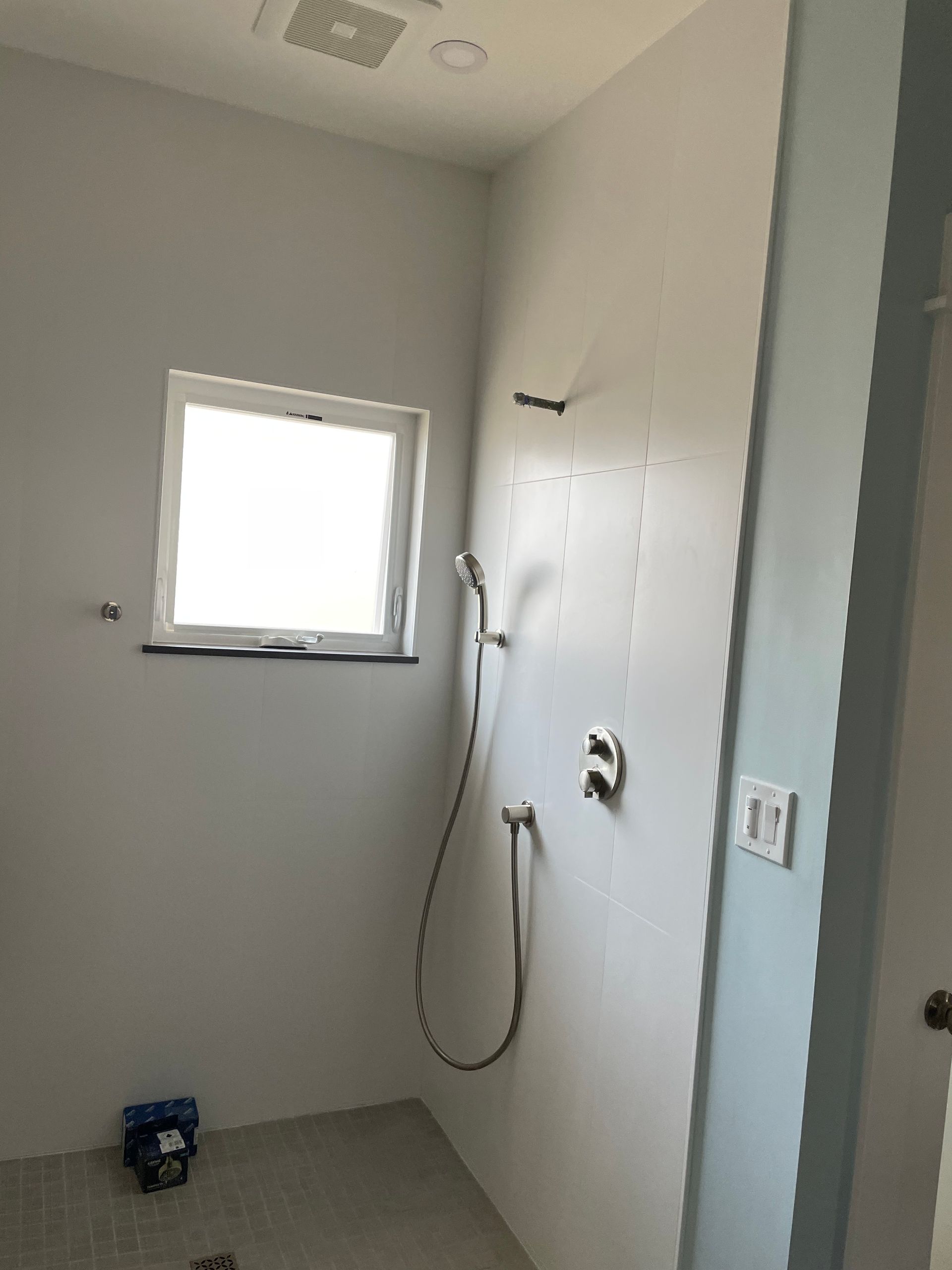 Small white tiled shower room with a window, handheld shower, and a soap dispenser on the wall.