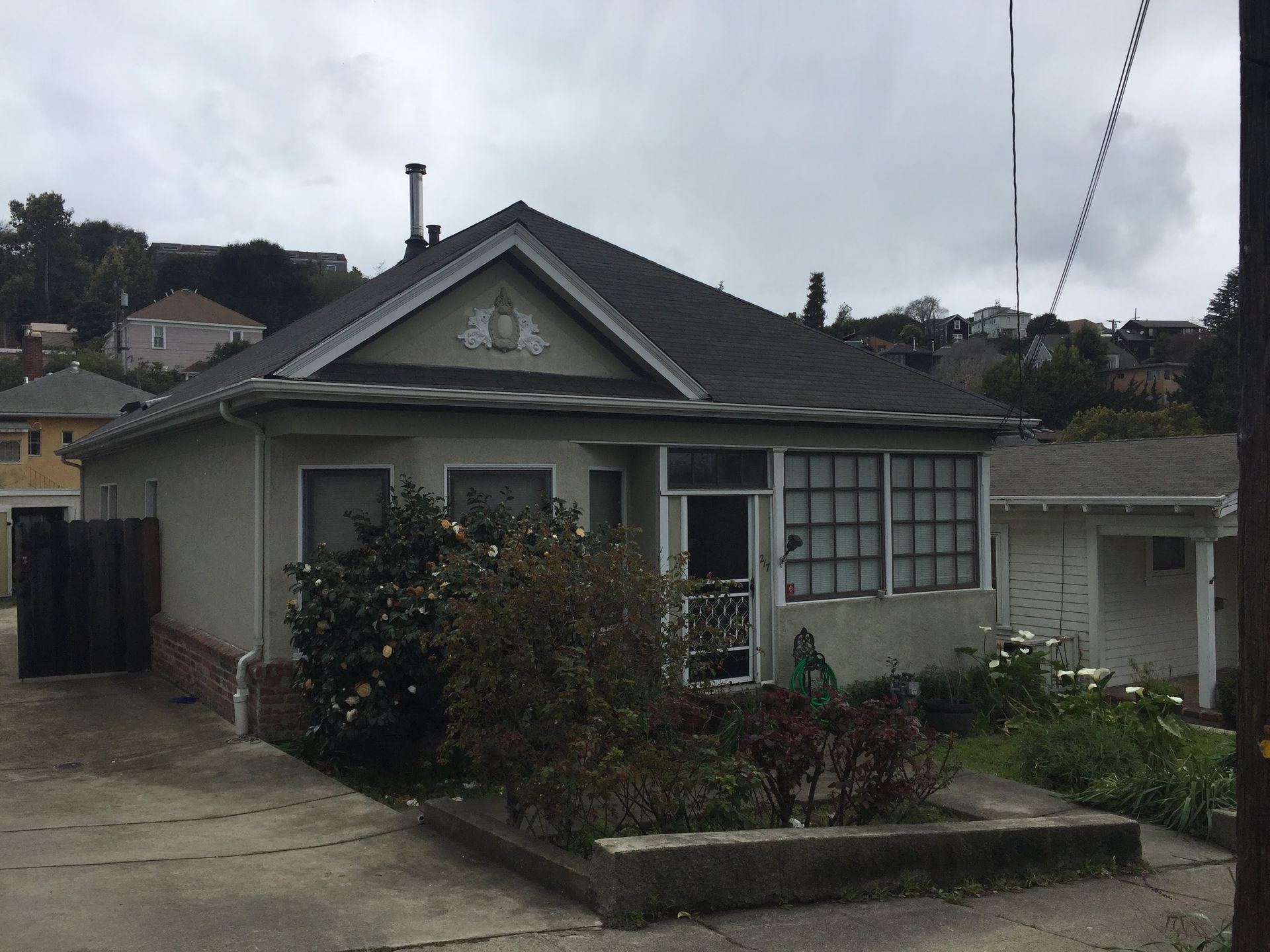 Single-story gray house with driveway, front garden, and cloudy sky.