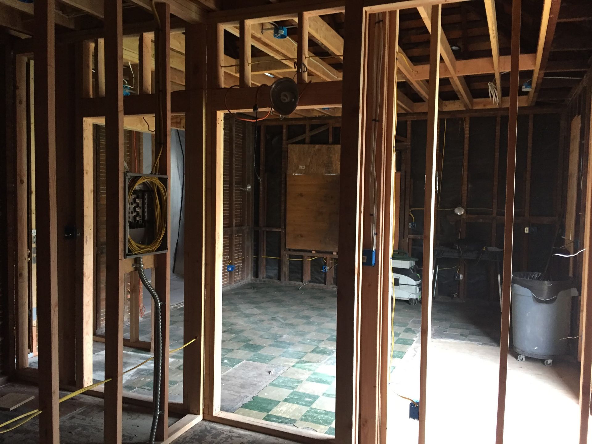 Unfinished interior with exposed wooden framing, wiring, and a checkered floor in a dim room.