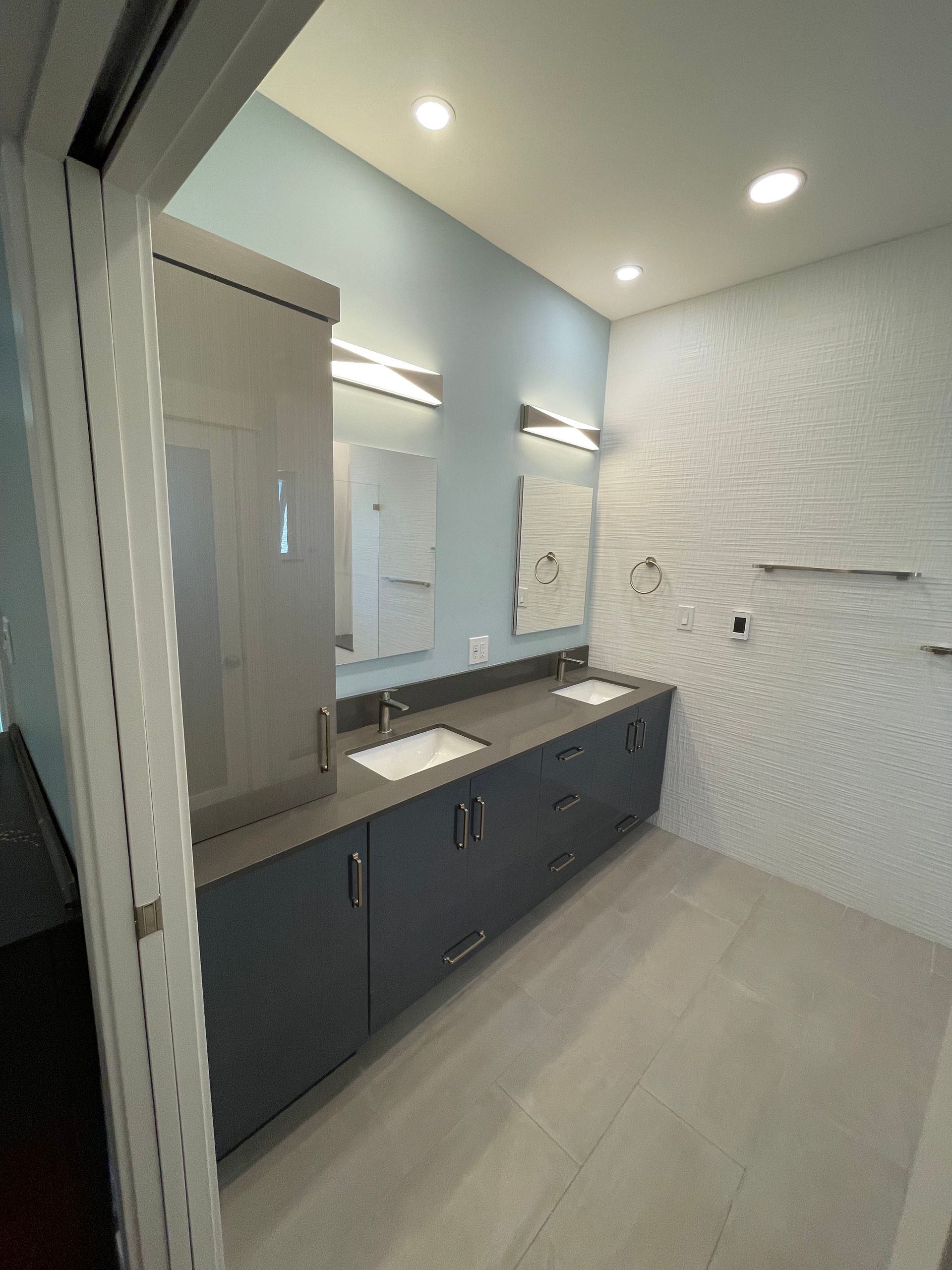 Modern bathroom with dark double vanity, large mirror, white tile walls, and recessed ceiling lights