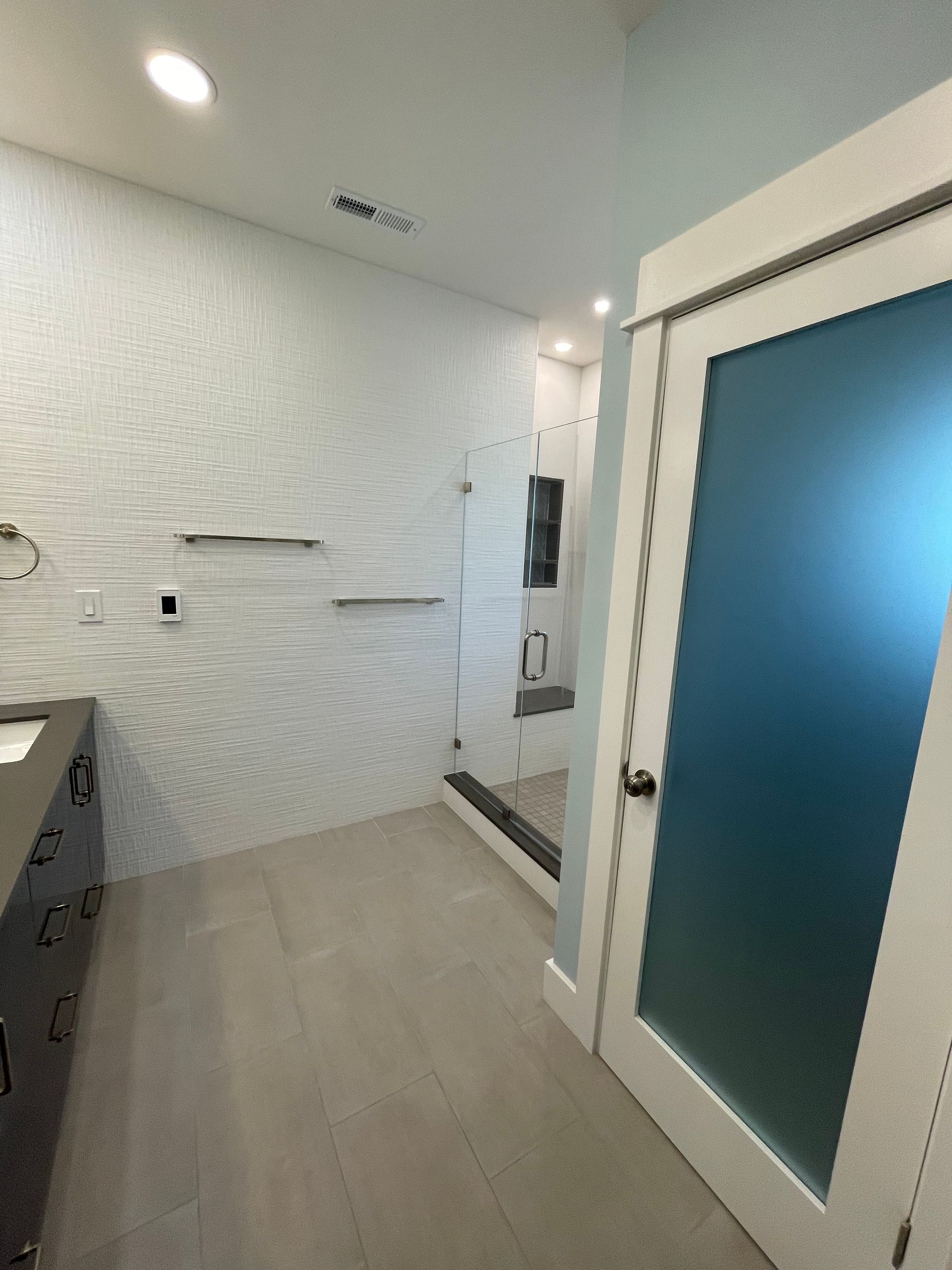 Bright modern bathroom with white walls, gray floor, vanity, and frosted glass shower door