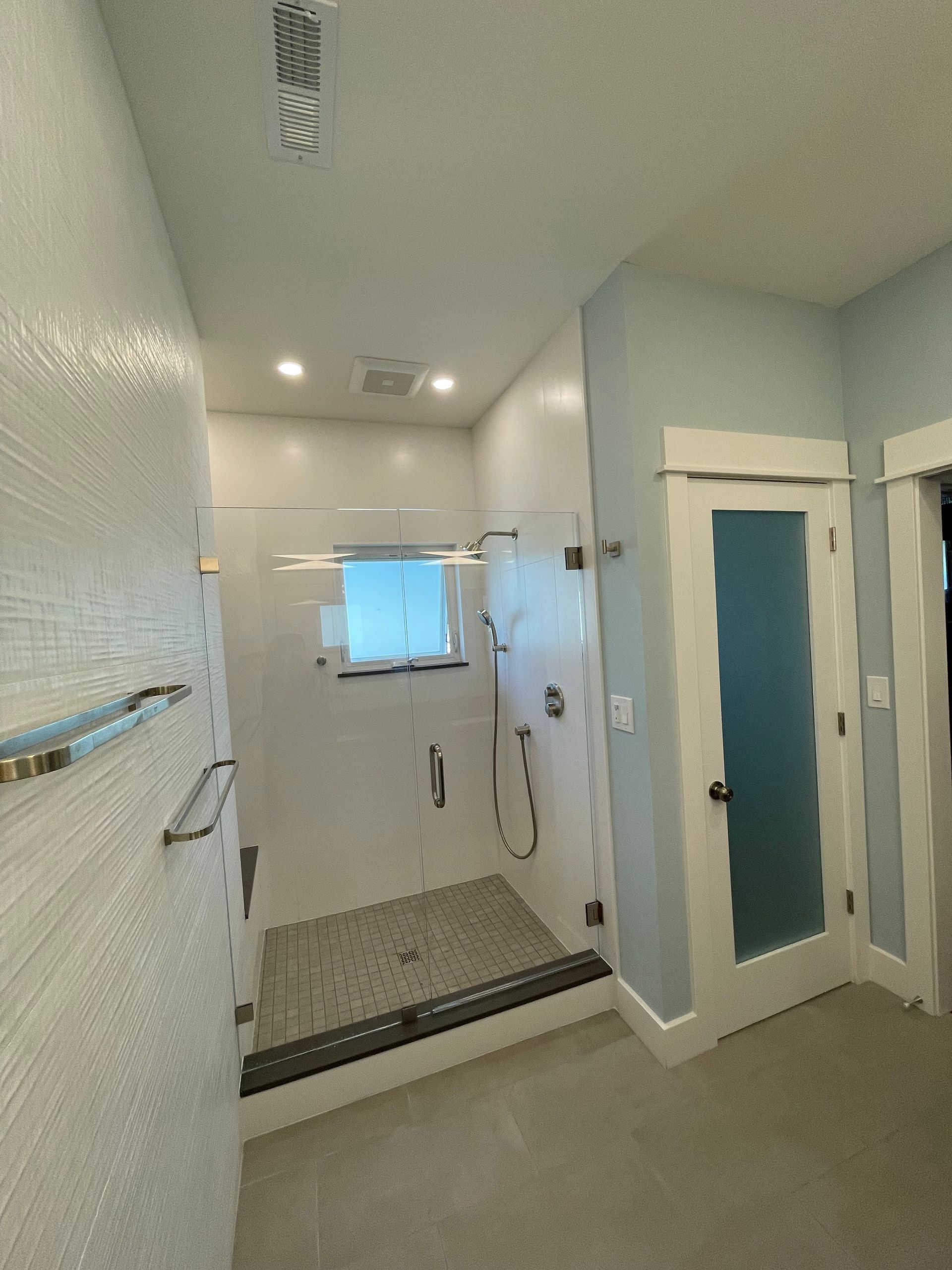 Accessible walk-in shower with glass door, grab bar, handheld shower, and blue walls in a bathroom.
