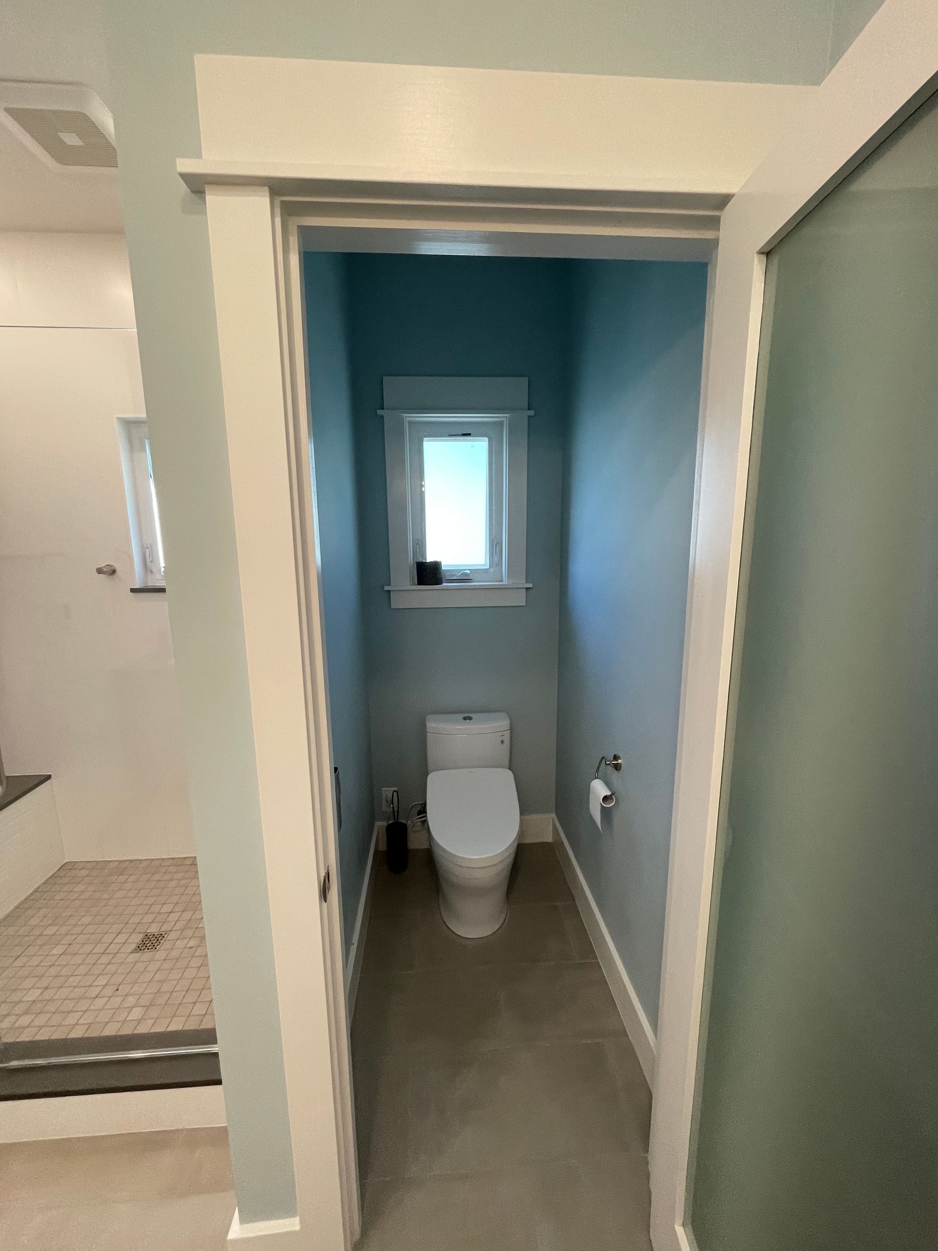 Small bathroom hallway with a toilet at the far end and blue walls.