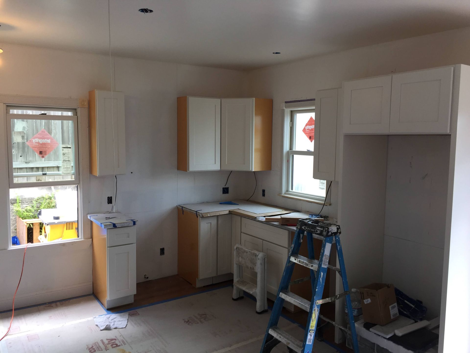 Unfinished kitchen with white cabinets, sink, ladder, and open window during renovation
