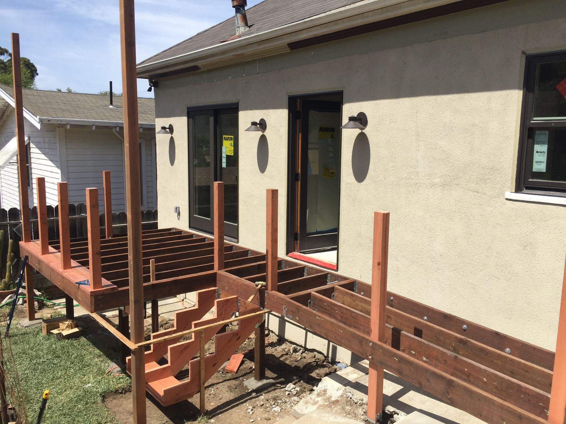 Raised wooden deck ramp under construction beside a beige house, with railings and support posts