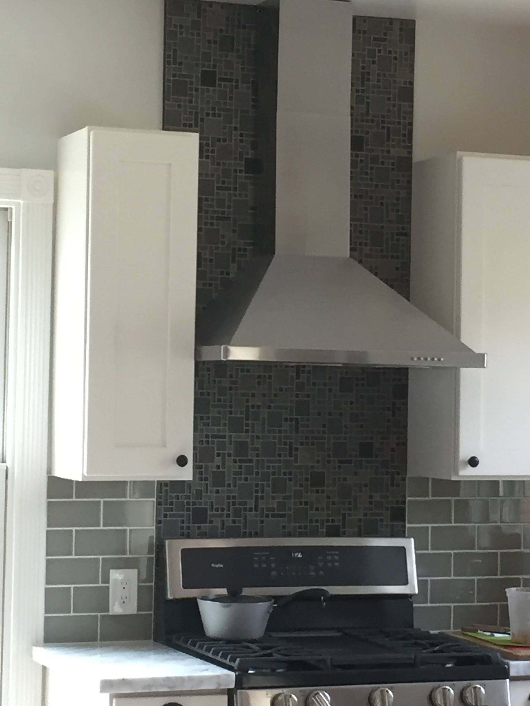 Modern kitchen stovetop with stainless range hood, white cabinets, and gray tile backsplash