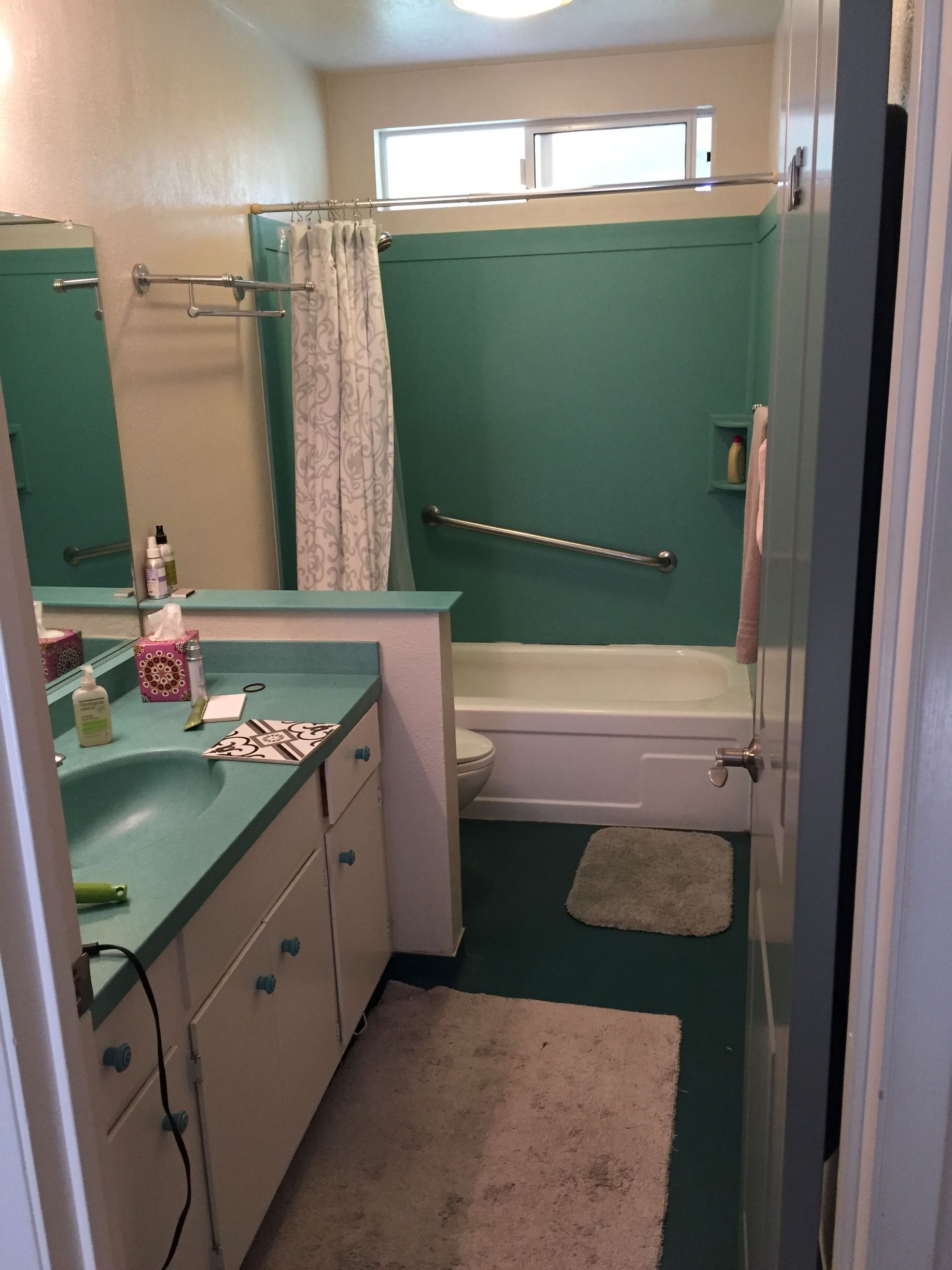 Small bathroom with green shower walls, beige walls, a sink cabinet, and rugs.