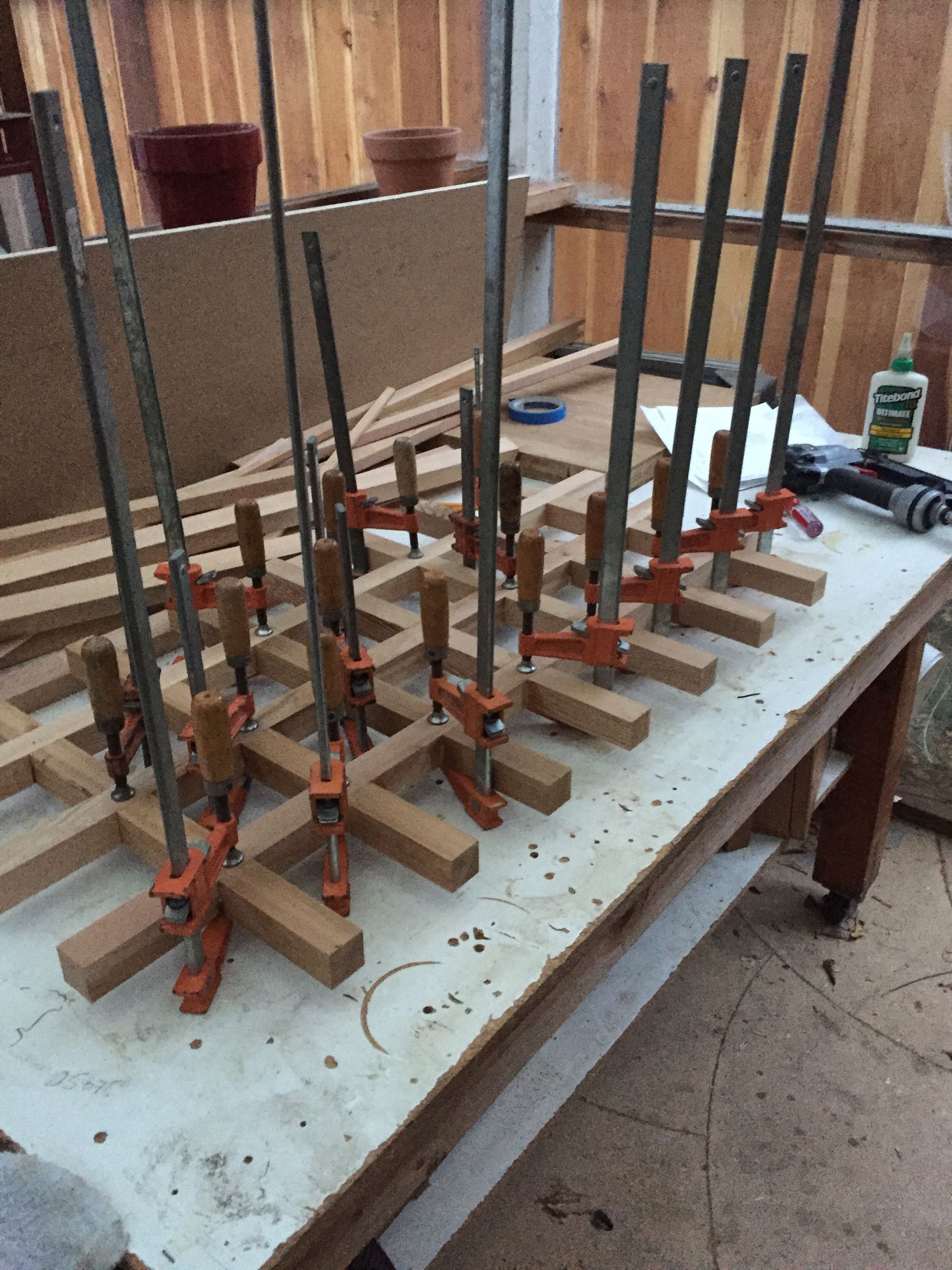 Several clamps hold wooden pieces and metal rods on a workbench in a workshop.