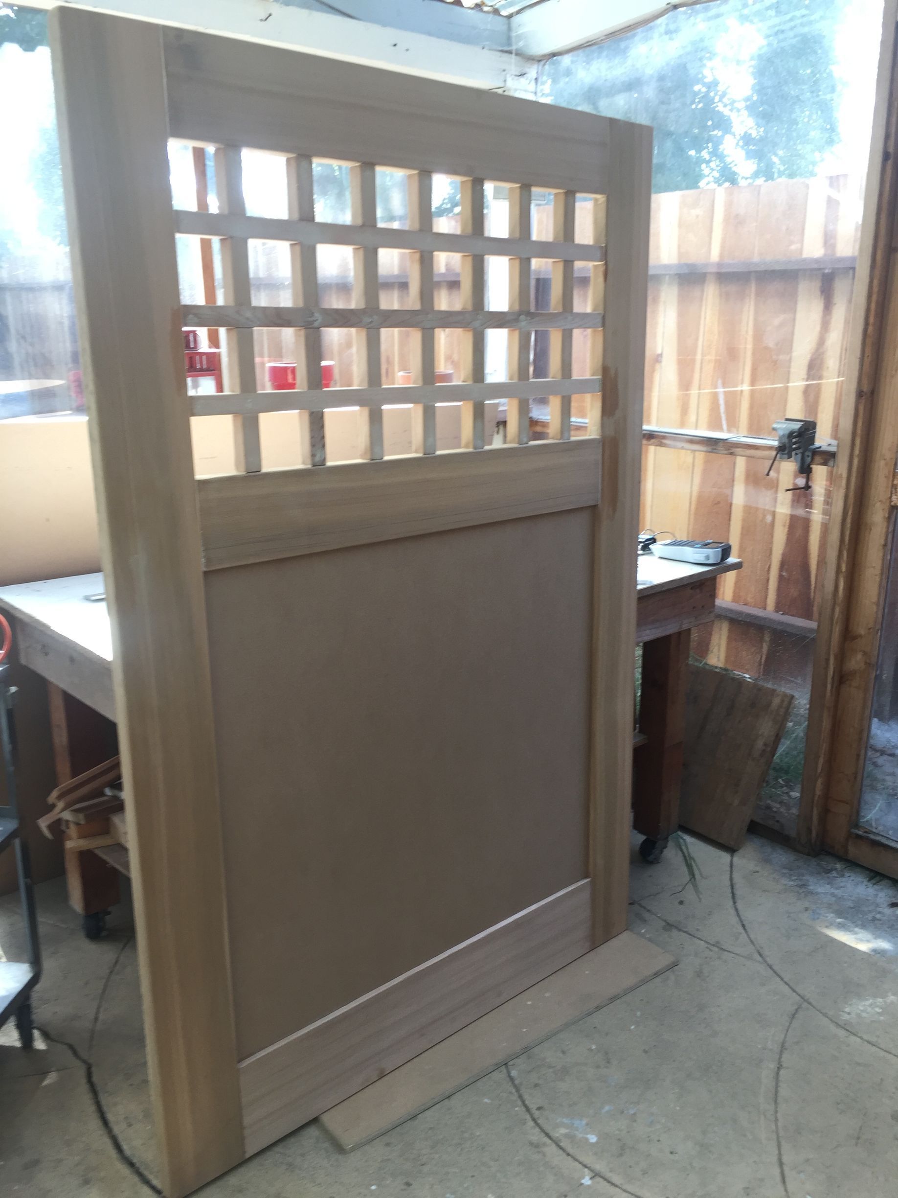 Wooden lattice privacy screen or partition in an outdoor patio with a fence and table behind it