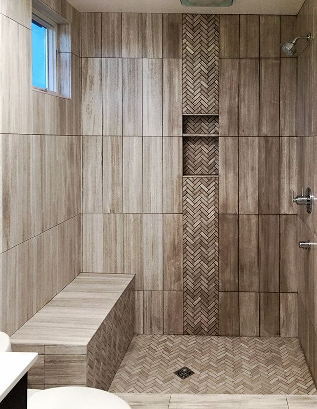 A bathroom with a walk in shower with a bench and a window.