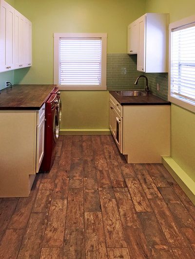 A kitchen with wooden floors , white cabinets , a sink , and a window.