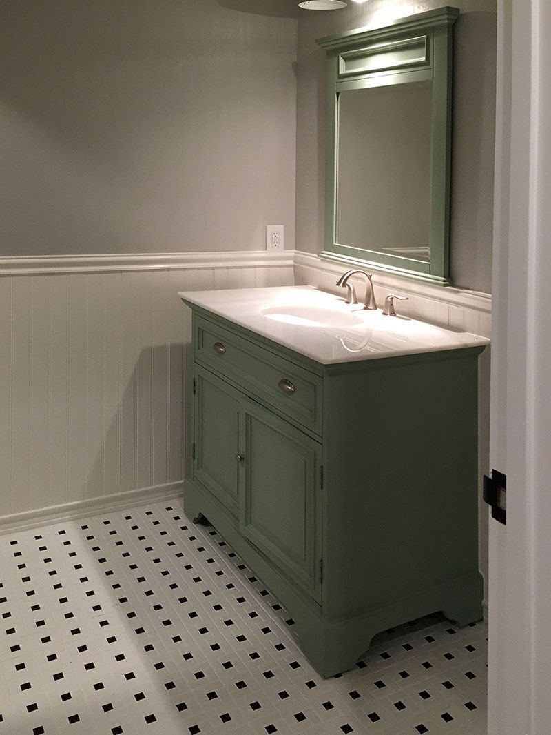 A bathroom with a green vanity and a mirror.