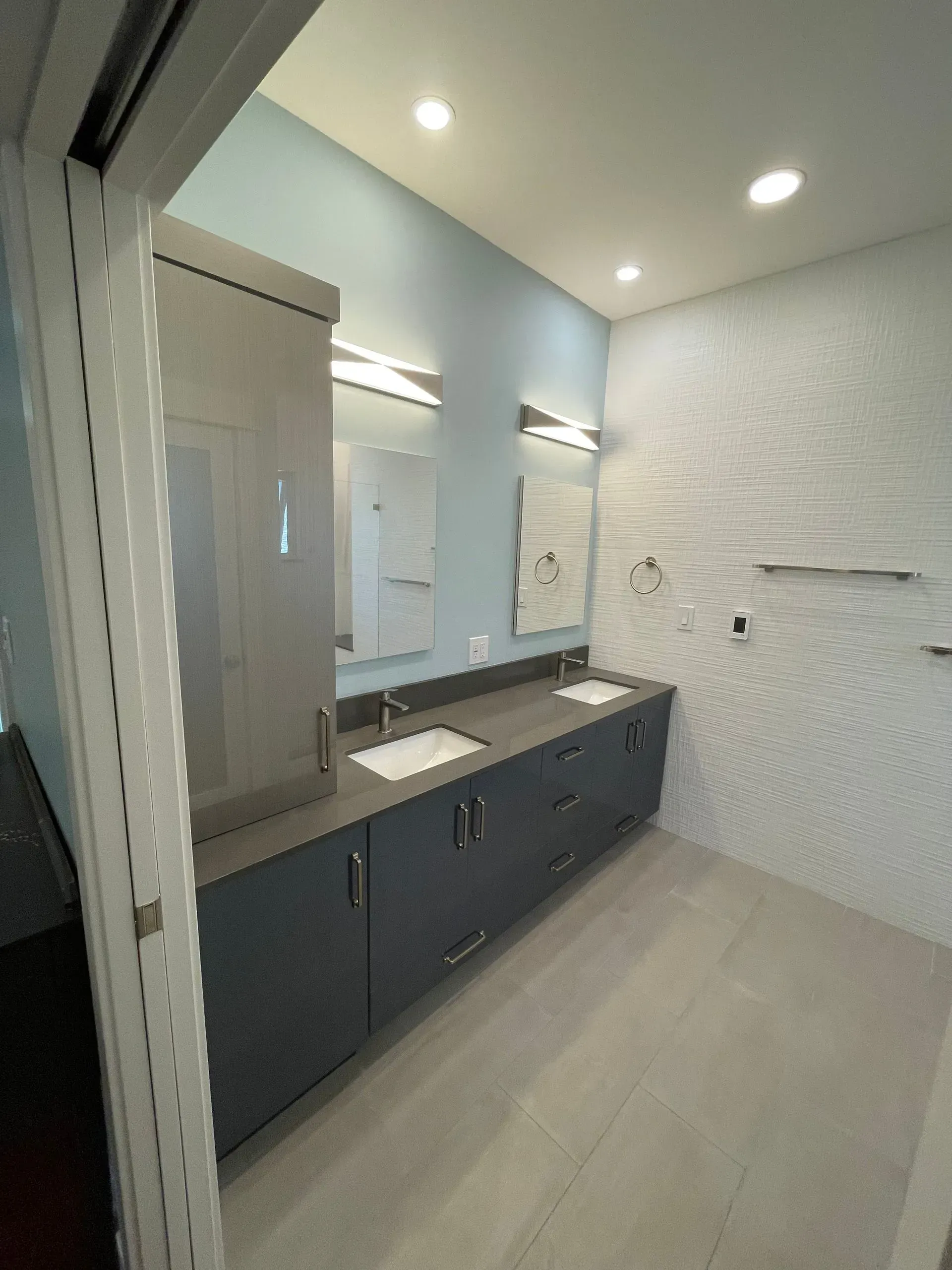 Modern bathroom with dark vanity, double mirrors, white textured walls, and bright ceiling lights