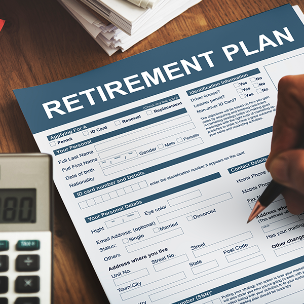 Person filling out a retirement plan form with a calculator on a wooden desk.