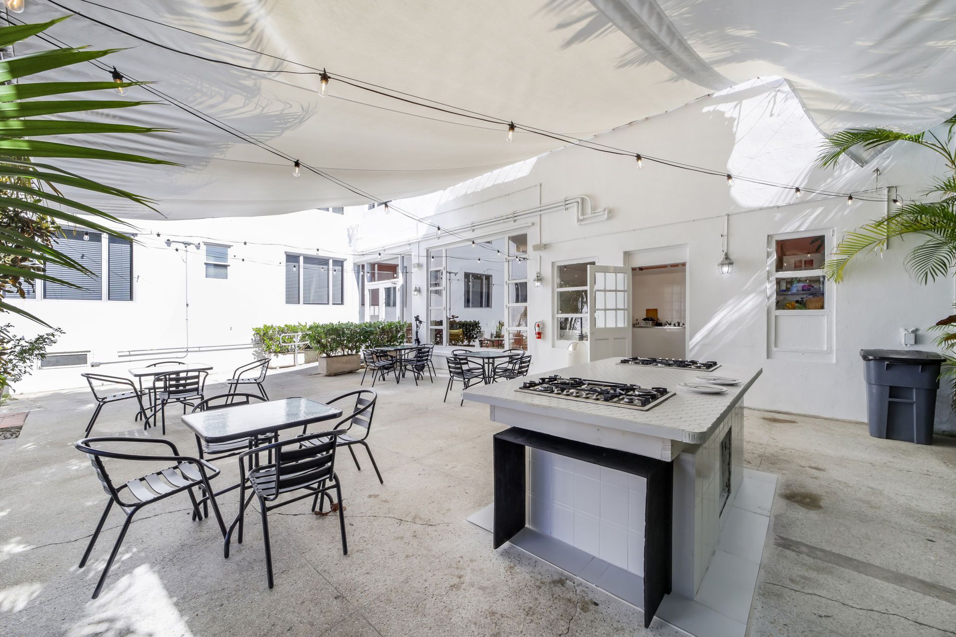 Outdoor patio with white canopy, tables and chairs, and a central serving island in a bright courtyard.