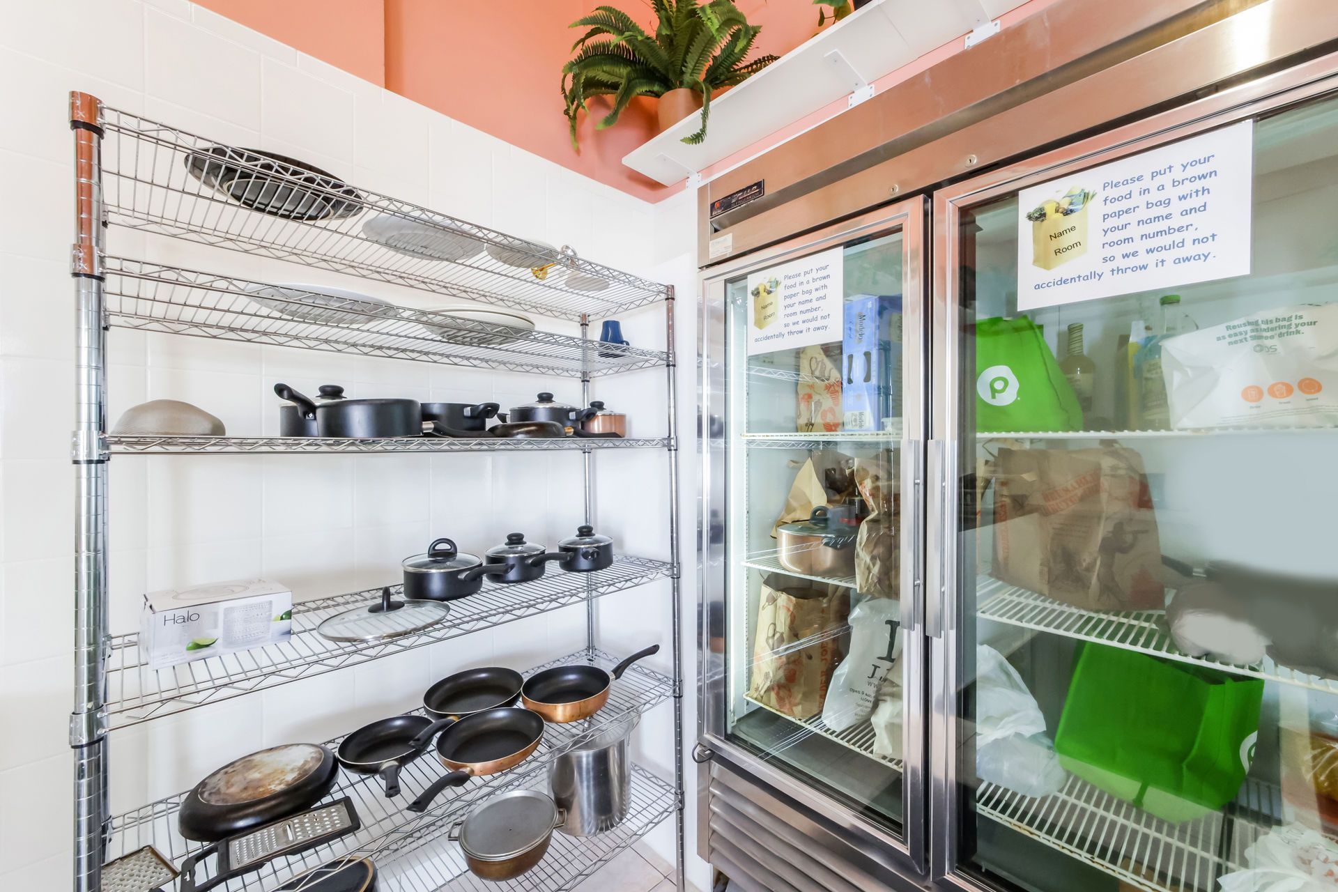 Shelves of pots and pans beside a glass-door refrigerator in a small kitchen or storage area