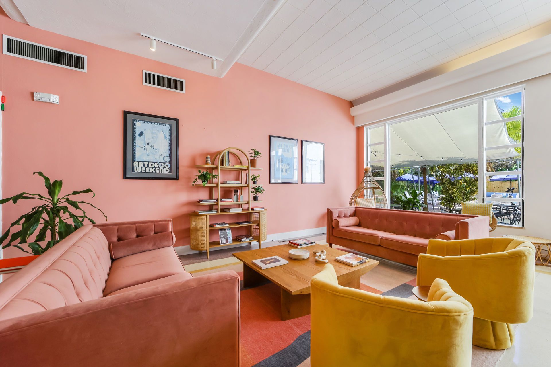 Pink living room with brown sofas, yellow chairs, and large windows overlooking greenery