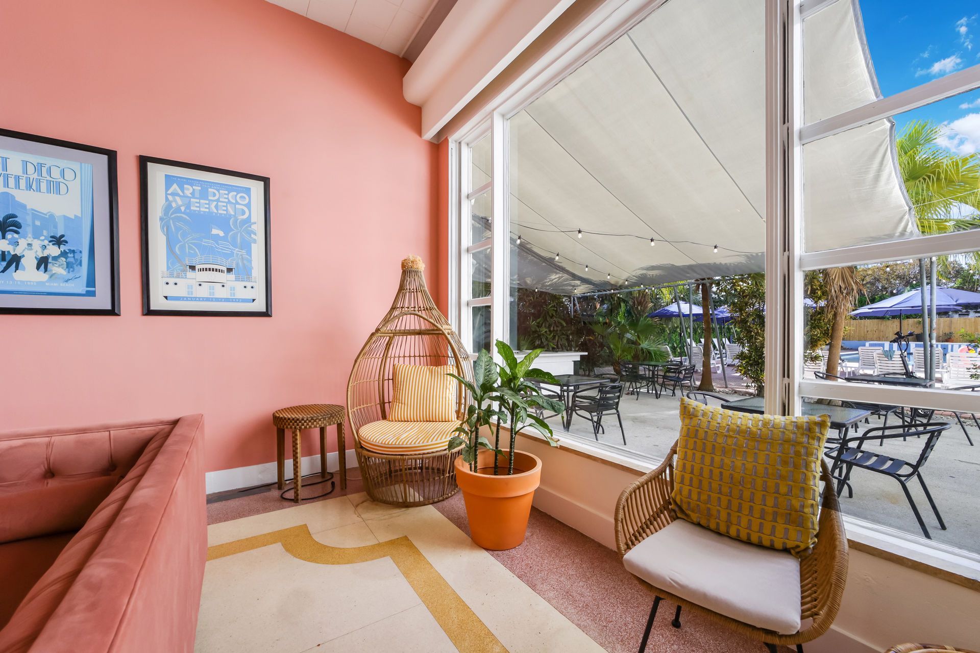 Bright pink sunroom with cushioned chair, wicker lantern, potted plant, and open view to patio outside
