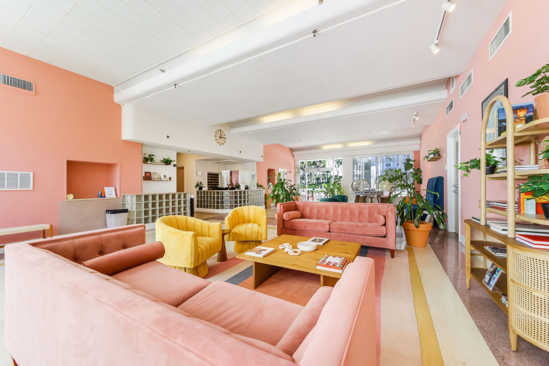 Bright, airy living room with pink sofas, yellow chairs, plants, and colorful decor on white floors.