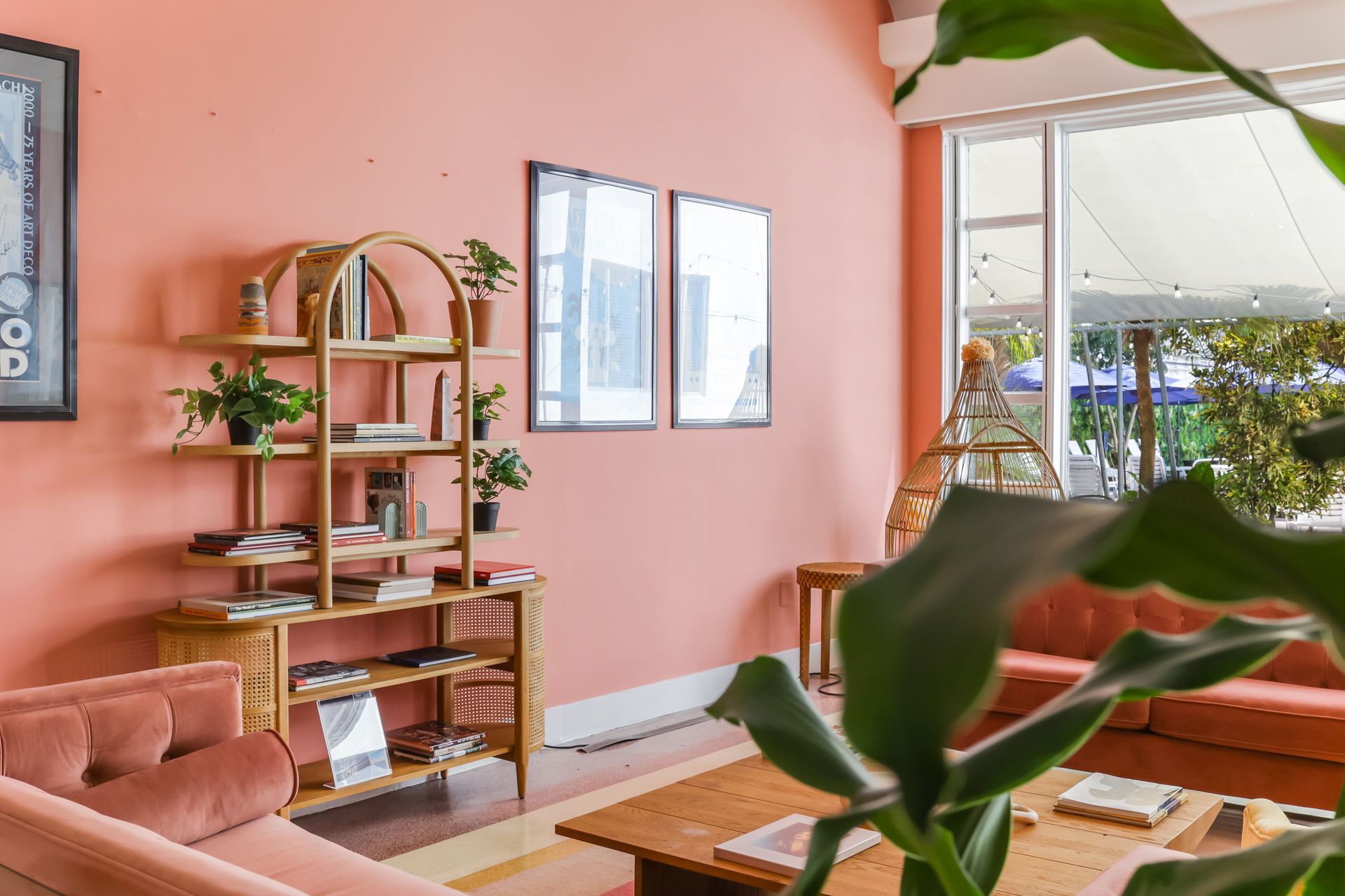 Cozy pink living room with wooden shelf, plants, sofa, and sunlight by a large window
