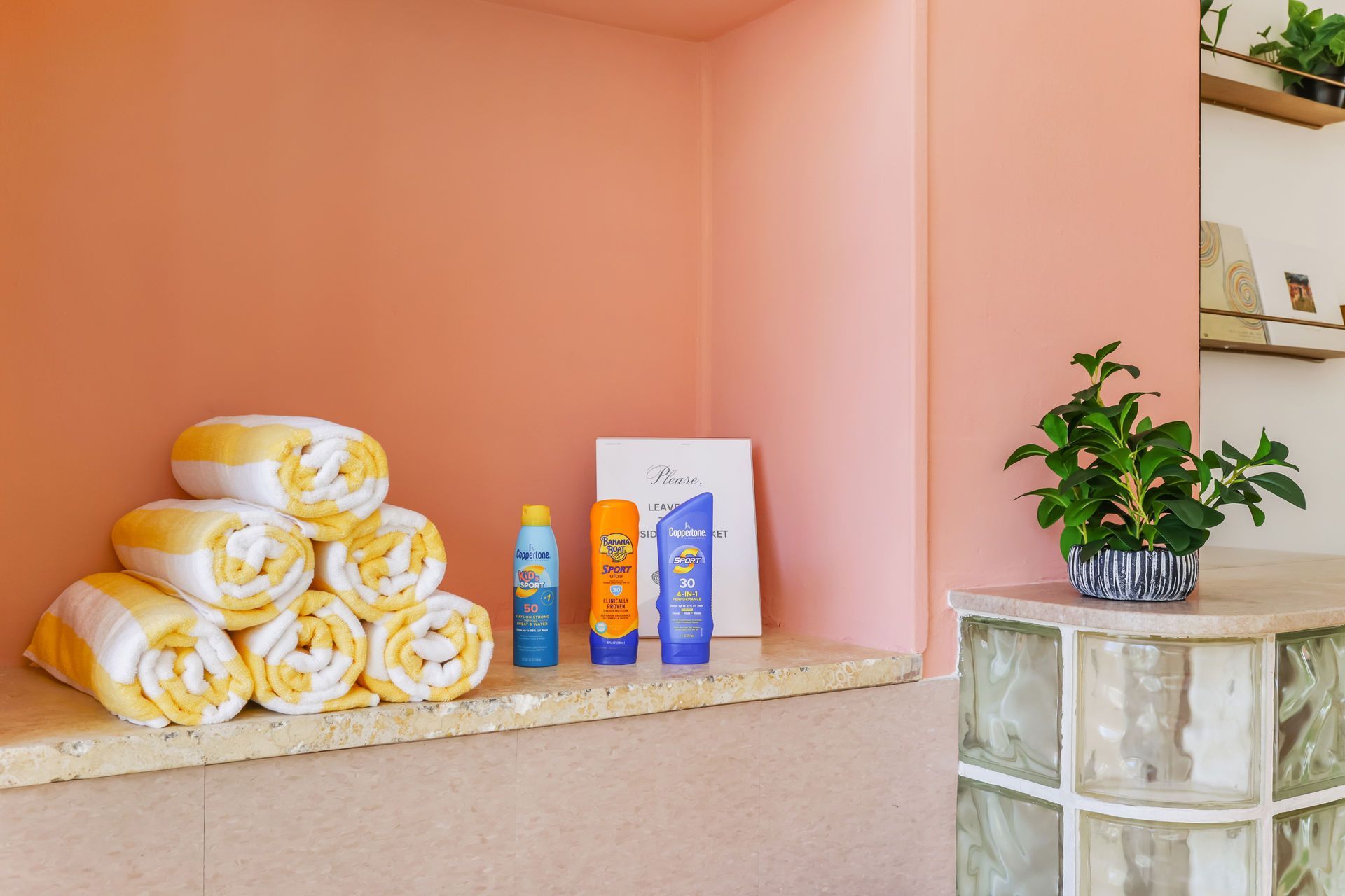 Stacked towels and toiletries on a shelf beside a potted plant in a pink spa-like alcove