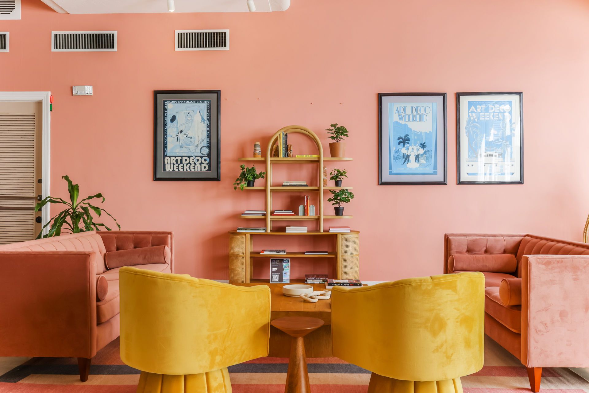 Modern living room with peach walls, orange sofas, yellow chairs, and framed art on the wall