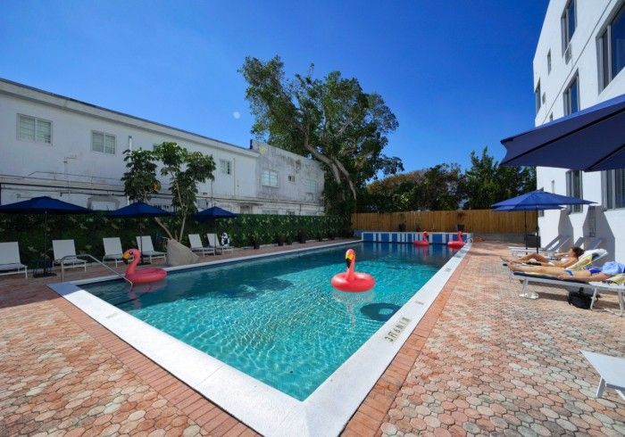 Outdoor swimming pool with clear blue water, lounge chairs, and red float rings beside a white building