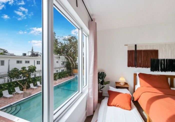 Bright bedroom with orange bedding and window view of a turquoise pool and palm trees