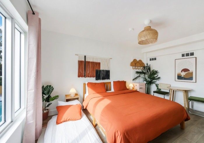 Bright bedroom with orange bedding, white walls, large window, and cozy decor.