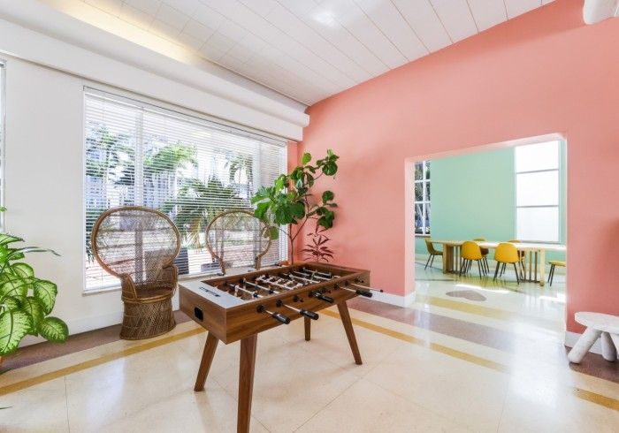 Bright living room with pink walls, wooden table, wicker chairs, and doorway to a yellow dining area