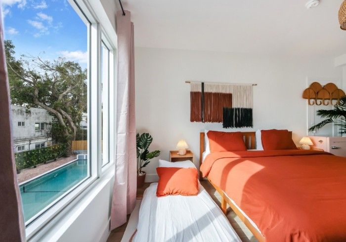 Bright bedroom with orange bedspread and window view of a swimming pool