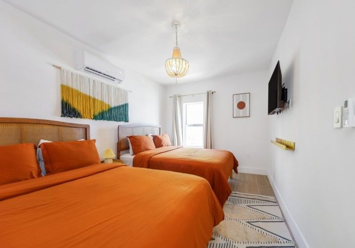 Bright bedroom with two orange beds, white walls, and a window at the far end