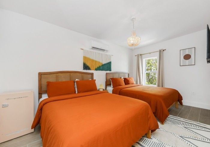 Bright bedroom with two orange-covered beds, white walls, and a window