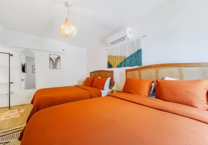 Bright bedroom with two orange beds, wicker headboard, and white walls
