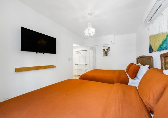 Orange bed and TV in a bright white bedroom with a wall shelf and window curtains