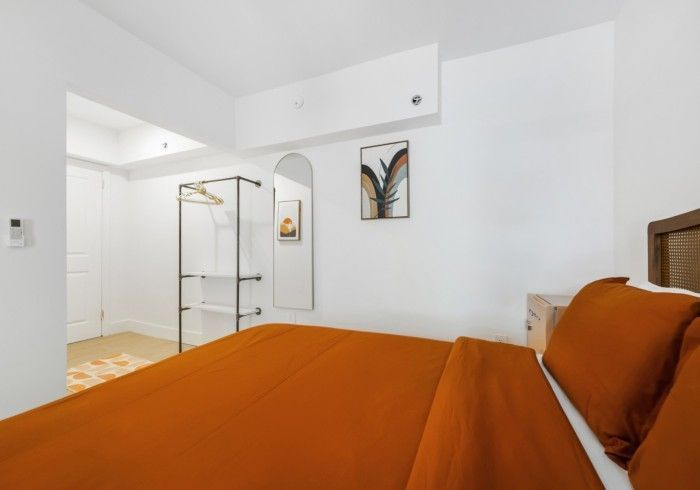 Bright bedroom with orange bedding, white walls, and a glass wardrobe near a doorway