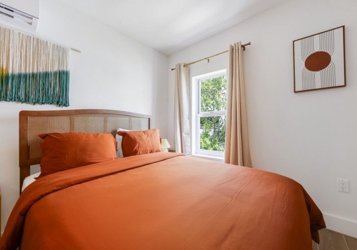 Bright bedroom with orange bedspread, wooden headboard, and a window with curtains
