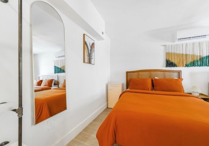 Bright bedroom with orange bedspread, mirror on wall, and arched doorway