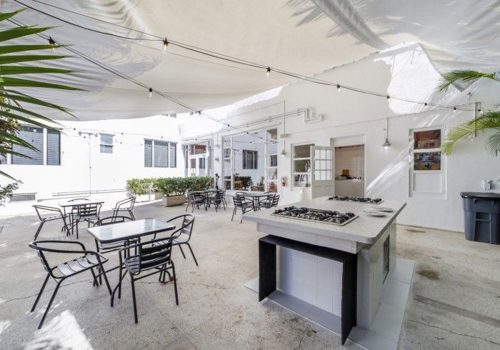 Outdoor patio with white canopy, tables, chairs, and a grill in a bright courtyard