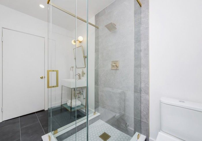 Modern bathroom with glass shower enclosure, white walls, and a toilet beside a vanity mirror.