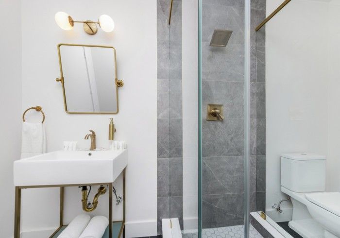 Bright white bathroom with gold fixtures, vanity sink, mirror, shower, and toilet.