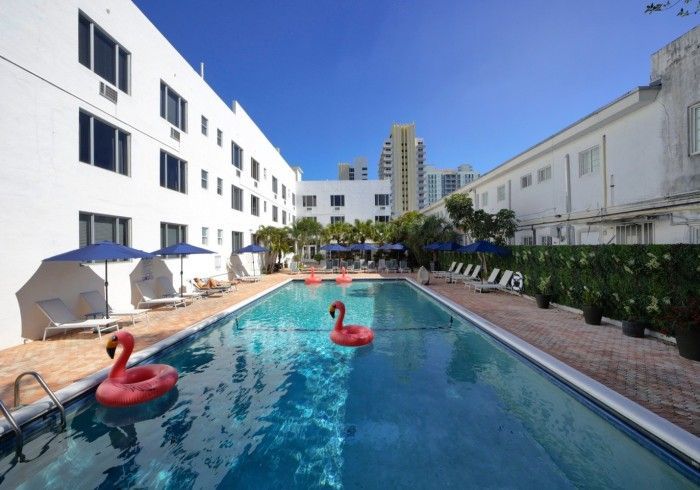 Outdoor hotel pool with two red flamingo floaties beside white buildings and lounge chairs