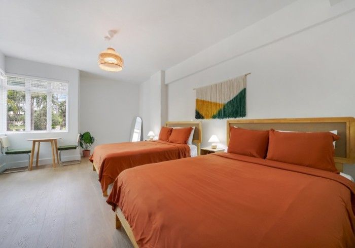 Bright bedroom with two orange beds, a window desk, and minimalist decor