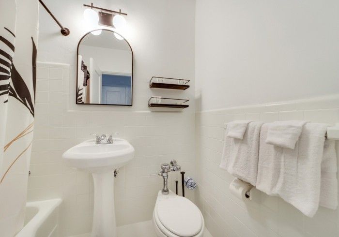 Small white bathroom with pedestal sink, mirror, toilet, and towels on the wall