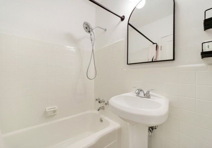 Small white bathroom with bathtub, wall-mounted sink, mirror, and showerhead on tiled walls.