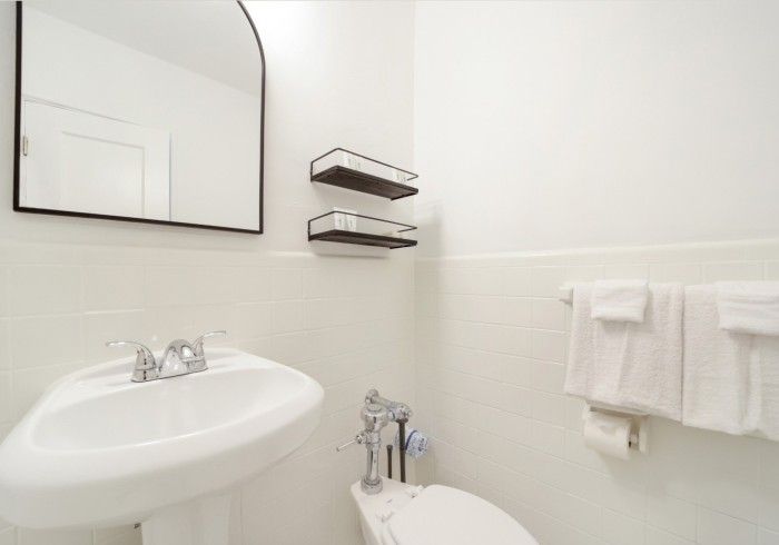 Bright white bathroom with sink, mirror, toilet, shelves, and towels on the wall