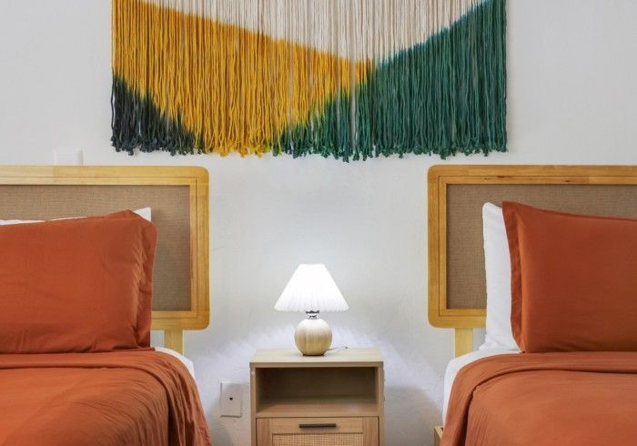 Two rust-orange beds with wooden headboards flank a nightstand and lamp, beneath a green and gold wall hanging.