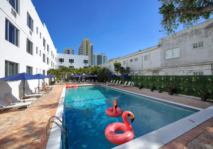 Outdoor hotel pool with pink float rings, lounge chairs, and white buildings under a blue sky